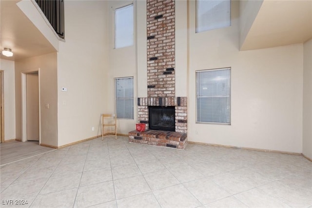 unfurnished living room with a high ceiling, light tile patterned floors, and a brick fireplace