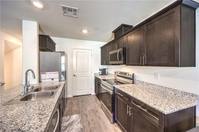 kitchen with visible vents, a sink, stainless steel appliances, light wood-style floors, and dark brown cabinetry