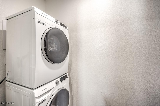 clothes washing area with laundry area, a textured wall, and stacked washer and dryer