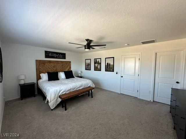 carpeted bedroom with a textured ceiling, visible vents, and a ceiling fan