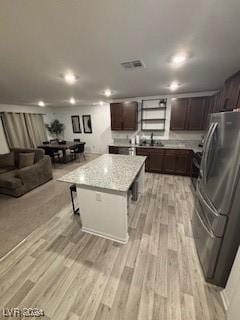 kitchen with visible vents, dark brown cabinets, light wood-type flooring, freestanding refrigerator, and a center island