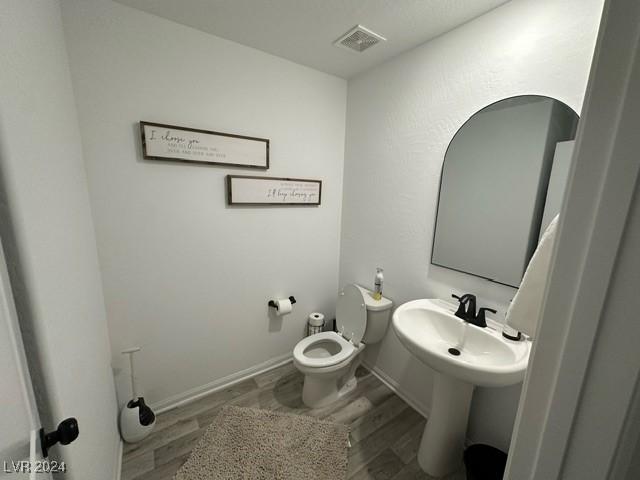 half bath featuring baseboards, visible vents, toilet, wood finished floors, and a sink