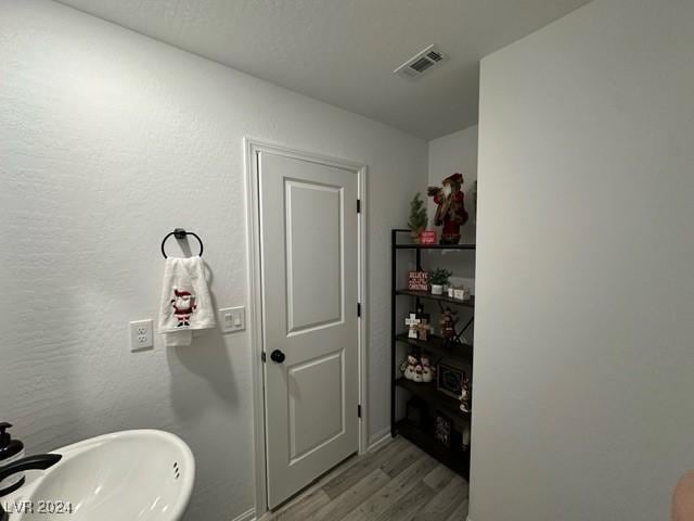 bathroom featuring a textured wall, wood finished floors, a sink, and visible vents