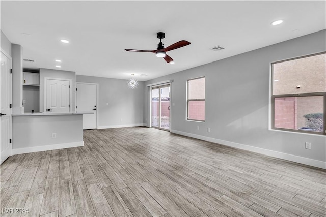 unfurnished living room featuring light wood-type flooring and ceiling fan with notable chandelier