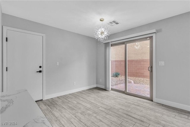 empty room featuring light wood-type flooring and an inviting chandelier