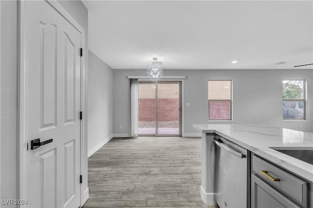 kitchen with gray cabinetry, light stone counters, stainless steel dishwasher, and light wood-type flooring