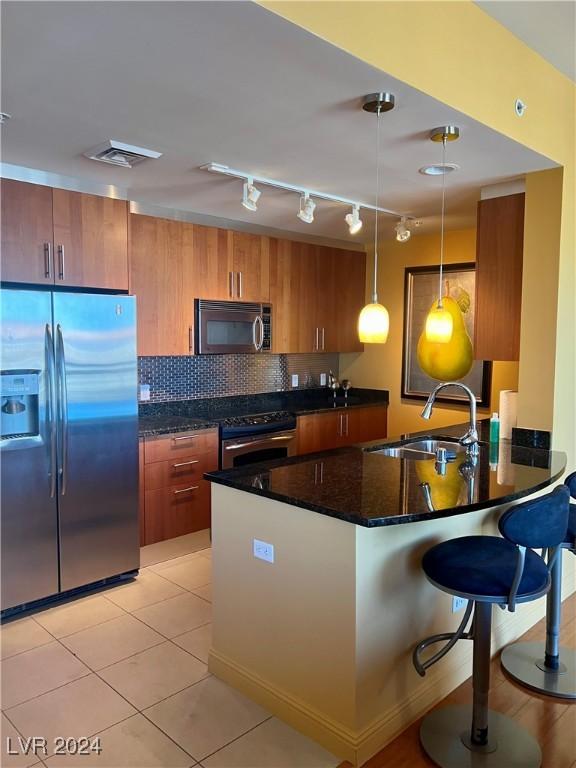 kitchen with pendant lighting, sink, appliances with stainless steel finishes, tasteful backsplash, and a breakfast bar area