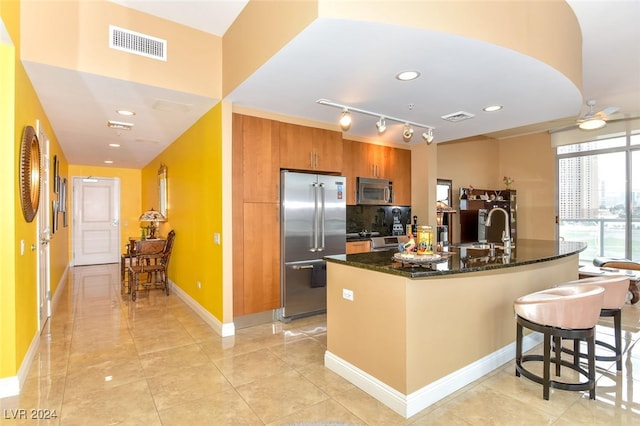 kitchen with a kitchen bar, rail lighting, dark stone counters, stainless steel appliances, and sink