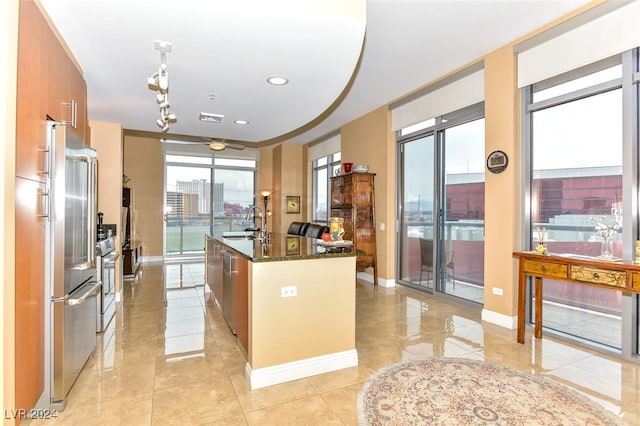 kitchen with high end fridge, dark stone counters, sink, range, and an island with sink