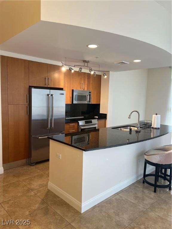 kitchen featuring a sink, stainless steel appliances, track lighting, light tile patterned floors, and dark countertops