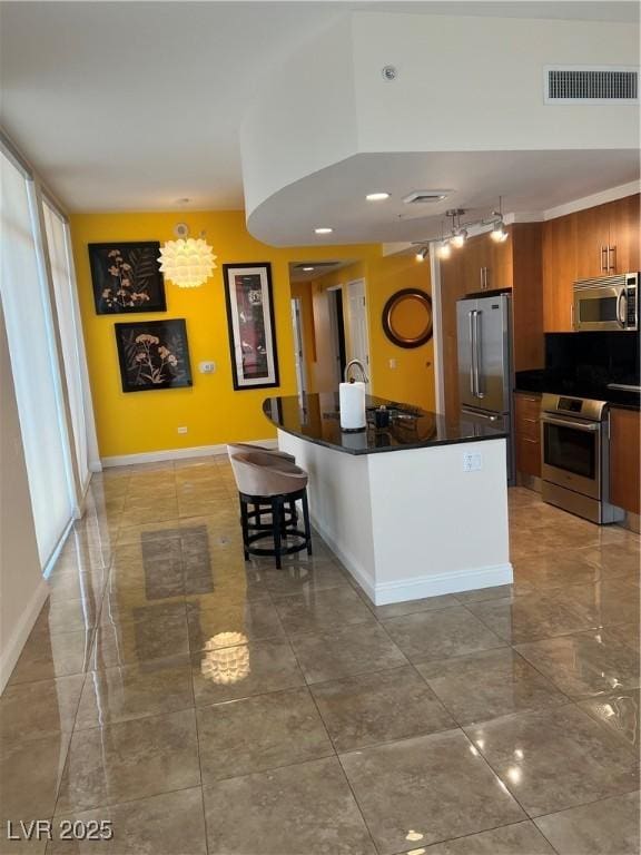 kitchen featuring a breakfast bar area, brown cabinets, dark countertops, stainless steel appliances, and visible vents