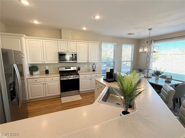 kitchen with an inviting chandelier, sink, hanging light fixtures, white cabinetry, and stainless steel appliances