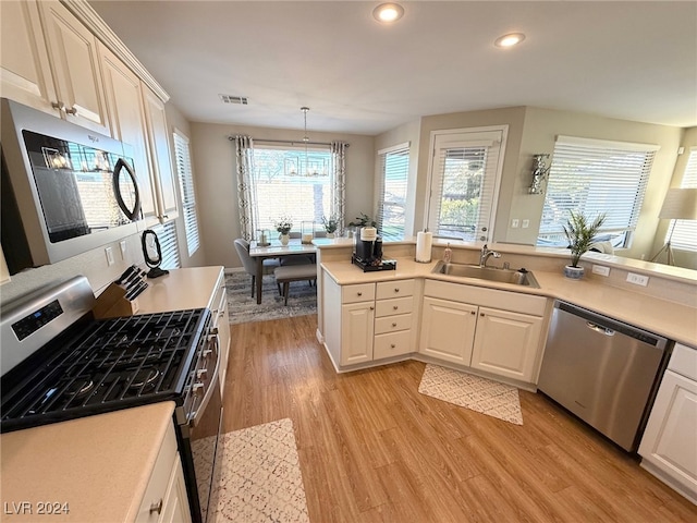 kitchen featuring white cabinetry, sink, decorative light fixtures, appliances with stainless steel finishes, and light wood-type flooring