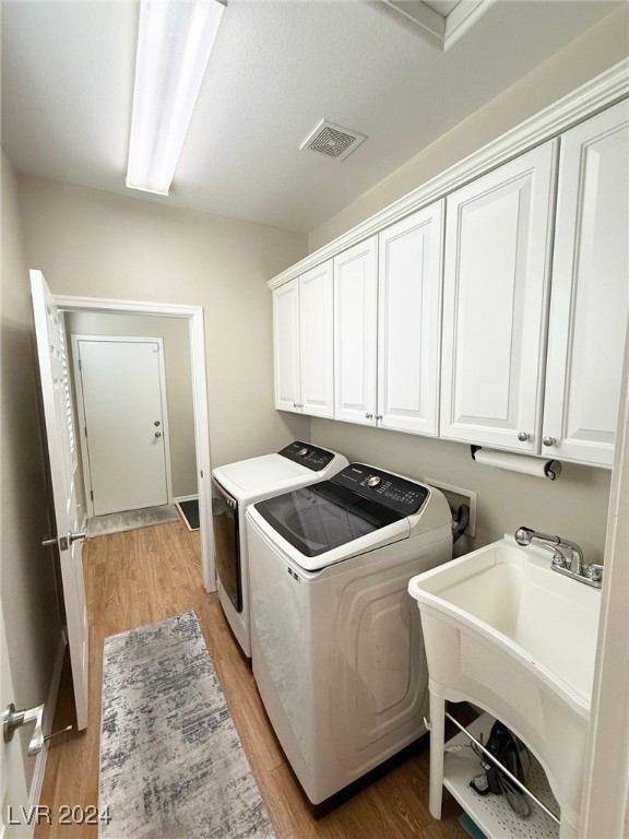 clothes washing area featuring cabinets, sink, washer and dryer, and wood-type flooring