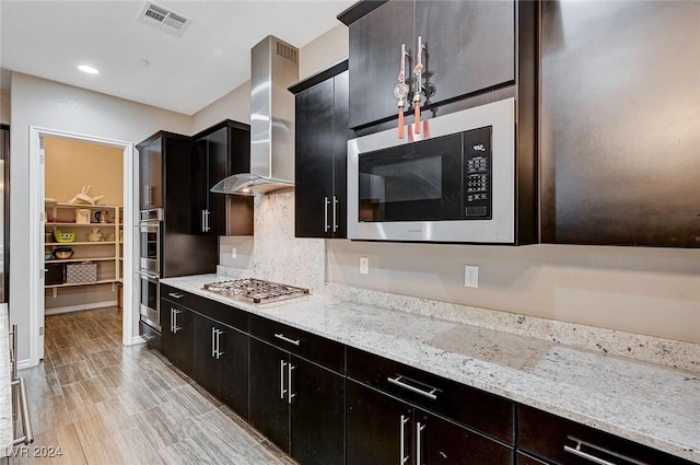 kitchen with light stone countertops, appliances with stainless steel finishes, decorative backsplash, and wall chimney range hood