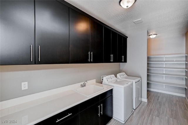 washroom with cabinets, sink, washer and dryer, light wood-type flooring, and a textured ceiling