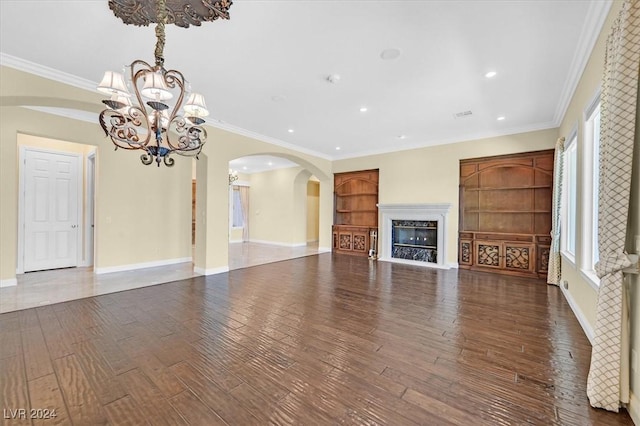 unfurnished living room with built in features, a high end fireplace, dark hardwood / wood-style floors, a notable chandelier, and crown molding