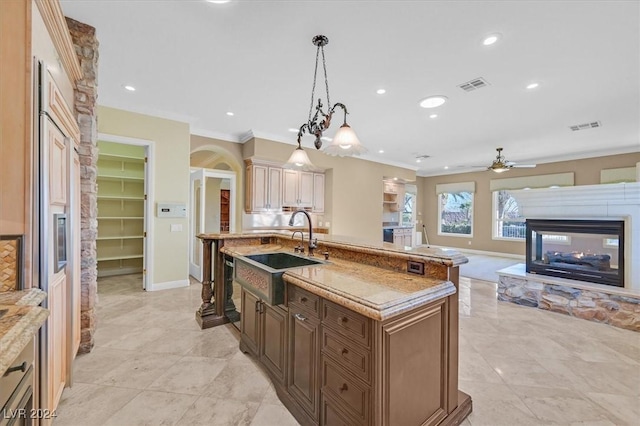 kitchen featuring ceiling fan, sink, a center island with sink, a fireplace, and hanging light fixtures