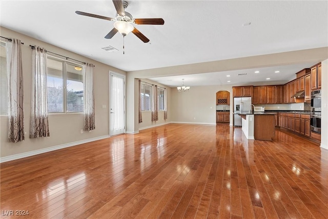 unfurnished living room with ceiling fan with notable chandelier and light wood-type flooring