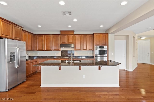 kitchen featuring a breakfast bar, dark hardwood / wood-style floors, dark stone countertops, a kitchen island with sink, and stainless steel appliances