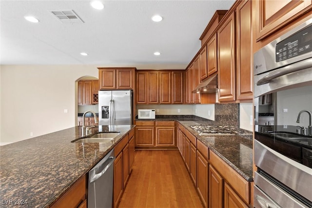 kitchen featuring sink, tasteful backsplash, light wood-type flooring, dark stone countertops, and stainless steel appliances