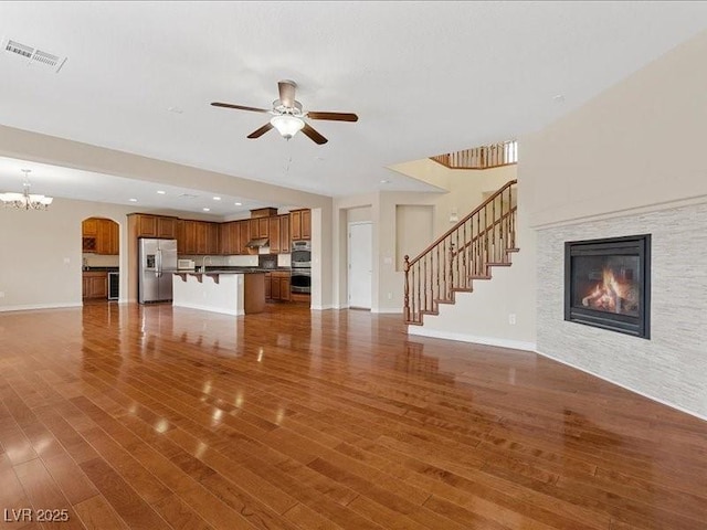 unfurnished living room featuring ceiling fan with notable chandelier and dark hardwood / wood-style flooring