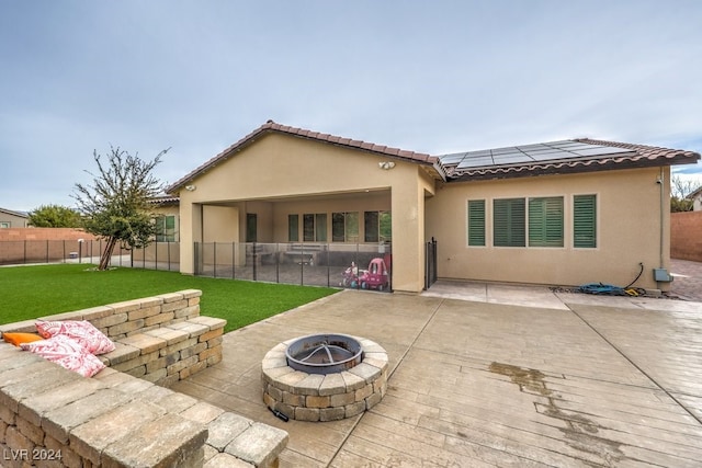 rear view of house featuring a lawn, a patio area, a fire pit, and solar panels