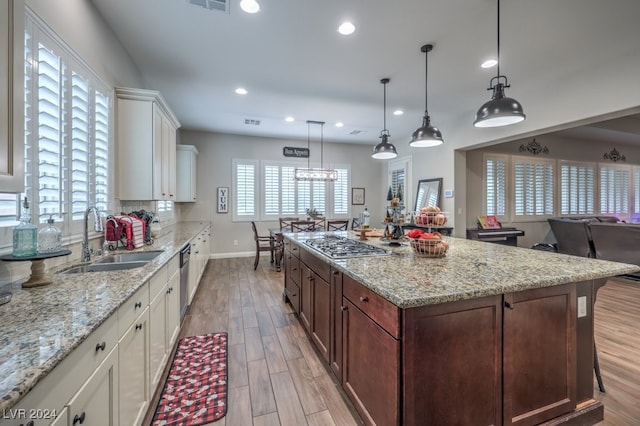 kitchen with white cabinetry, sink, hanging light fixtures, and light wood-type flooring