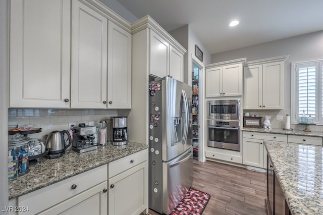 kitchen with tasteful backsplash, light stone counters, light hardwood / wood-style floors, white cabinets, and appliances with stainless steel finishes