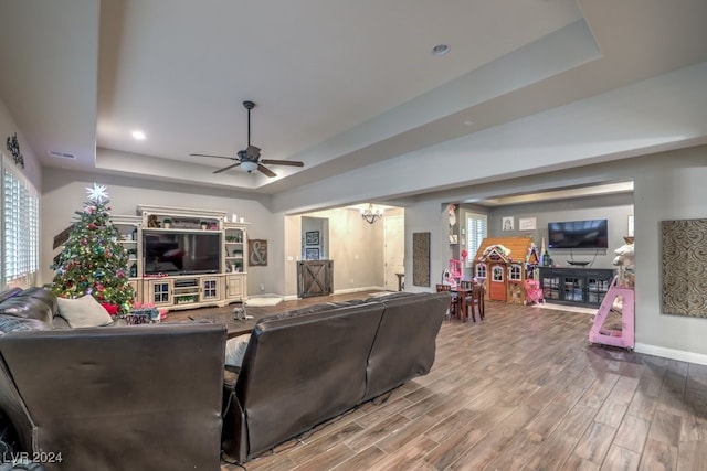 living room with wood-type flooring, a raised ceiling, a wealth of natural light, and ceiling fan