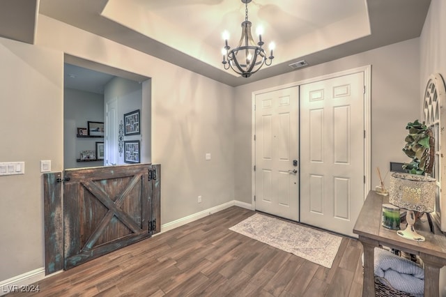 entrance foyer with a tray ceiling, dark wood-type flooring, and a chandelier