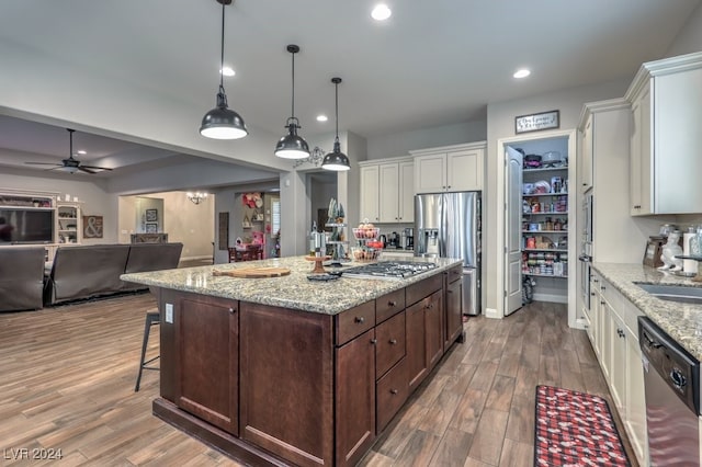 kitchen featuring white cabinets, a center island with sink, hanging light fixtures, light stone countertops, and appliances with stainless steel finishes