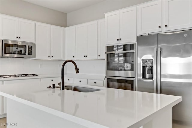 kitchen with white cabinets, appliances with stainless steel finishes, an island with sink, and sink