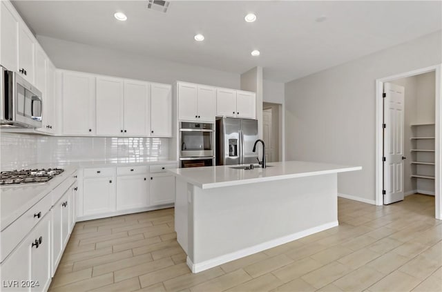 kitchen featuring a center island with sink, white cabinets, sink, decorative backsplash, and appliances with stainless steel finishes