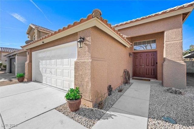 view of exterior entry with a tiled roof, stucco siding, an attached garage, and concrete driveway