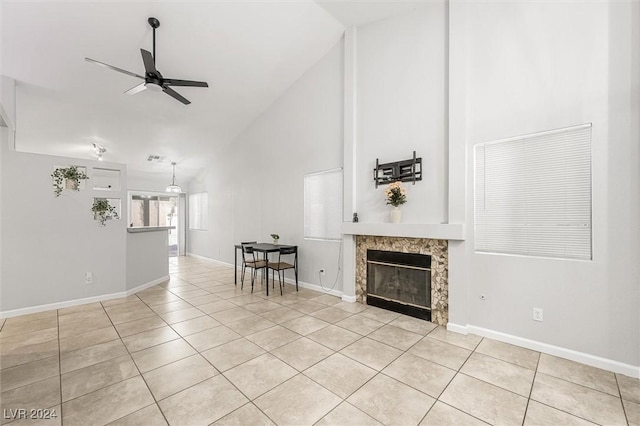 unfurnished living room featuring light tile patterned floors, baseboards, high vaulted ceiling, ceiling fan, and a tiled fireplace