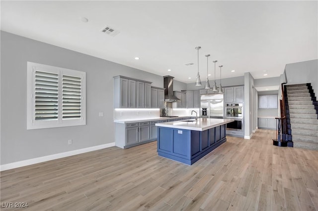 kitchen featuring wall chimney exhaust hood, stainless steel built in refrigerator, a breakfast bar, pendant lighting, and a center island with sink