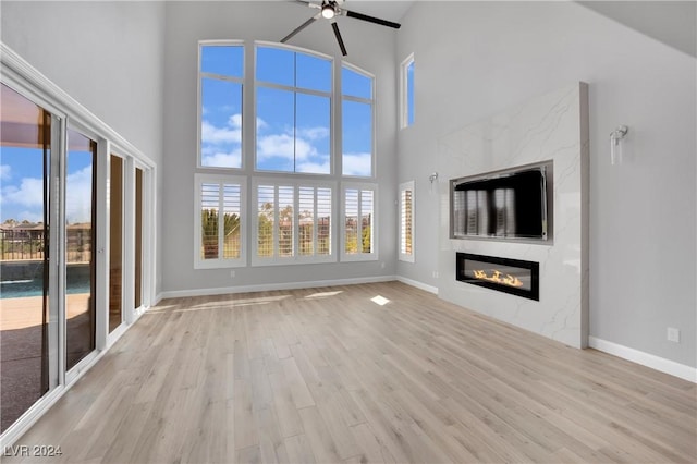 unfurnished living room with ceiling fan, a fireplace, high vaulted ceiling, and light wood-type flooring