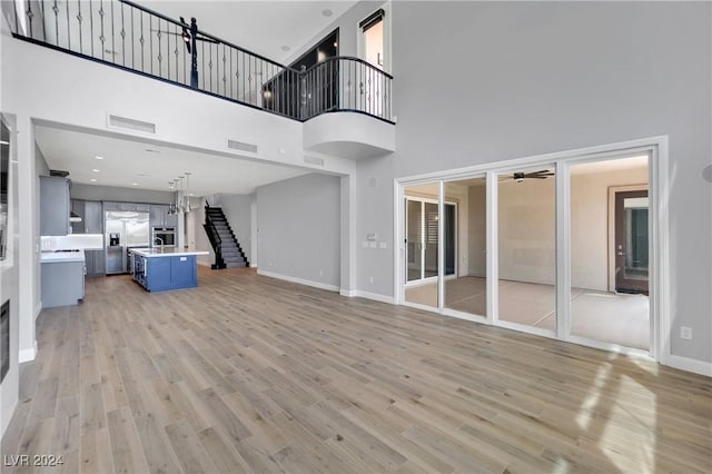 unfurnished living room featuring ceiling fan, light wood-type flooring, and a high ceiling