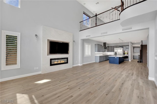 unfurnished living room with a towering ceiling, light hardwood / wood-style floors, and a premium fireplace