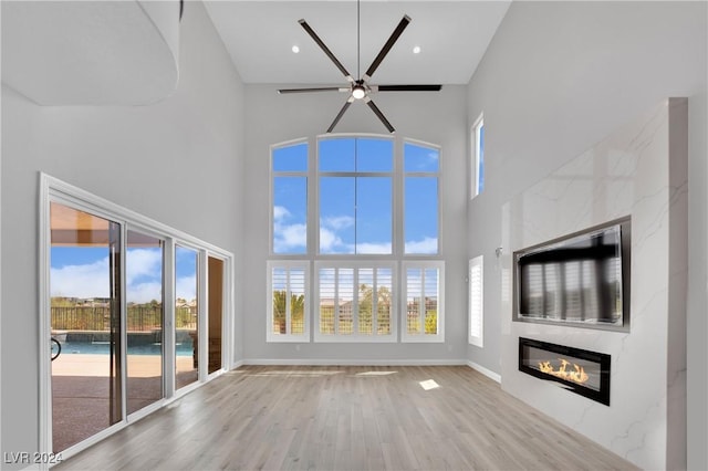 unfurnished living room with ceiling fan, light hardwood / wood-style floors, a fireplace, and a high ceiling