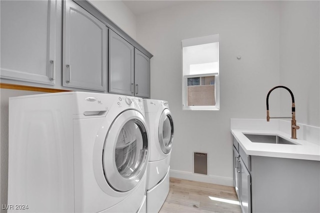 laundry area featuring cabinets, separate washer and dryer, light hardwood / wood-style flooring, and sink