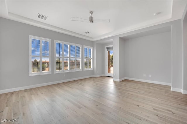 empty room featuring a tray ceiling, ceiling fan, and light hardwood / wood-style floors