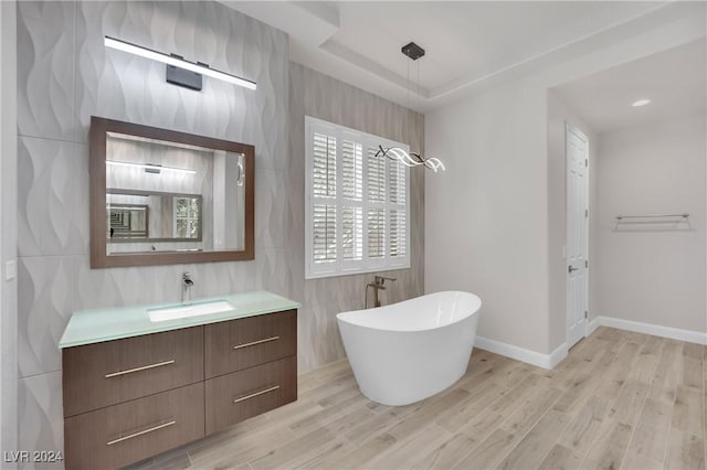 bathroom featuring a raised ceiling, a bathtub, vanity, tile walls, and hardwood / wood-style flooring