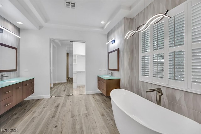 bathroom with a washtub, hardwood / wood-style floors, a tray ceiling, vanity, and tile walls