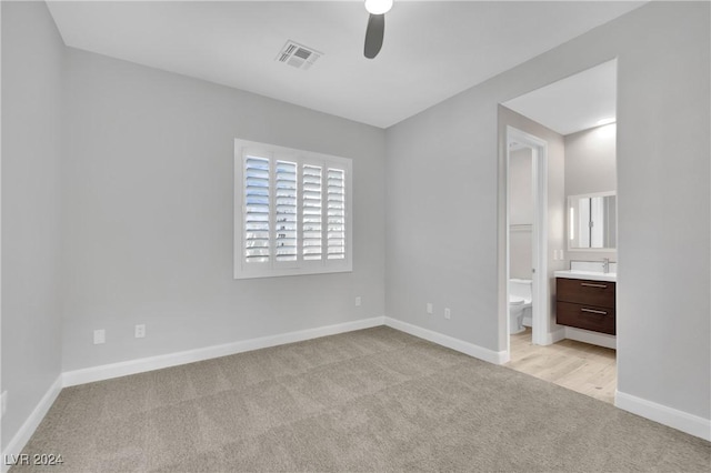 unfurnished bedroom featuring ensuite bathroom, ceiling fan, light colored carpet, and sink