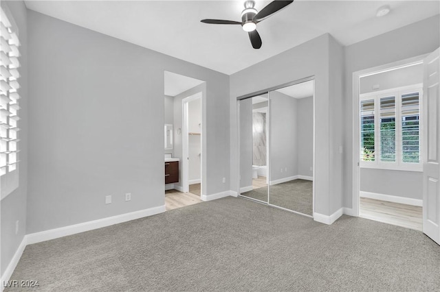 unfurnished bedroom featuring ceiling fan, ensuite bath, light colored carpet, and a closet