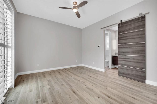 unfurnished room featuring ceiling fan, a barn door, a healthy amount of sunlight, and light hardwood / wood-style flooring