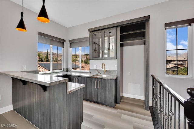 bar with light stone counters, sink, hanging light fixtures, and light hardwood / wood-style flooring