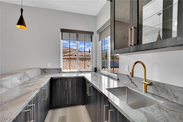 kitchen featuring light stone counters, sink, and decorative light fixtures